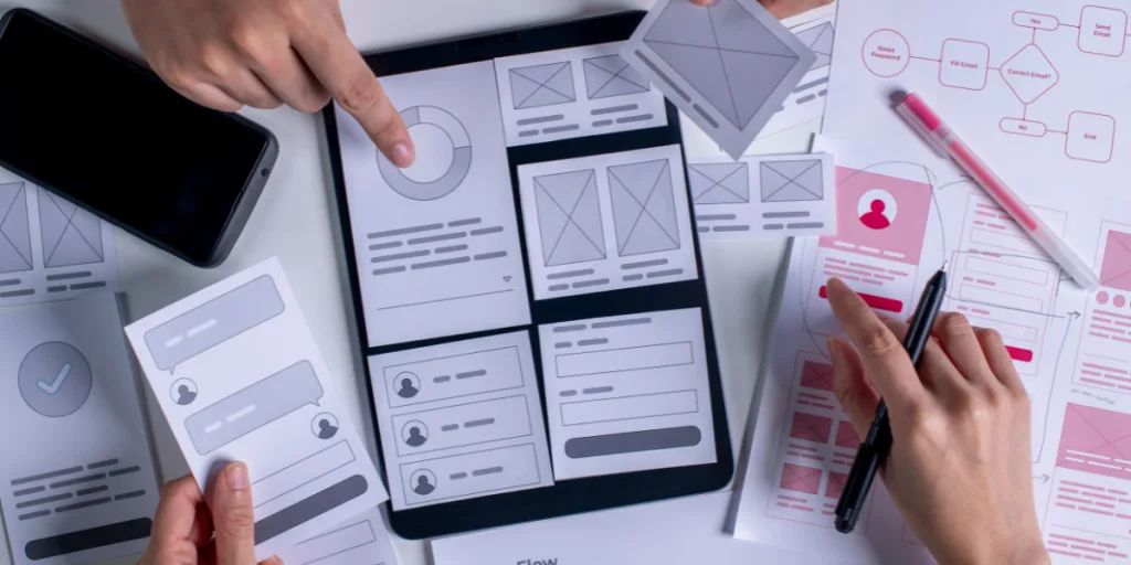 UX designers collaborating with wireframes and prototypes on a tablet and paper layouts — Make Your UX Research Hard To Ignore, web design Gold Coast.