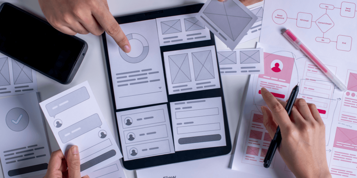 UX designers collaborating with wireframes and prototypes on a tablet and paper layouts — Make Your UX Research Hard To Ignore, web design Gold Coast.